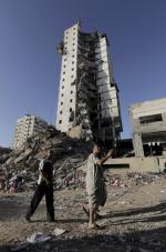 26일(현지시간) 팔레스타인 가자시티에서 두 남성이 전날 이스라엘군 공습으로 크게 파괴된, 이탈리아 건축회사 시공의 주상복합 아파트 옆을 지나고 있다. 연합