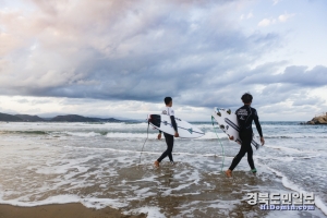 서핑동호인들이 파도를 탈 준비를 하며 바다로 걸어가고 있다.